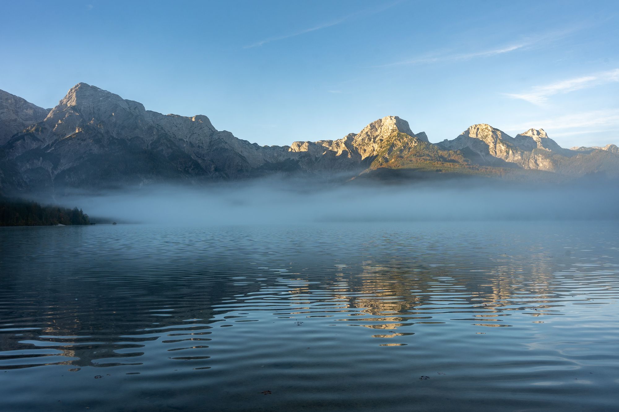 Mist over a still alpine lake with mountain peaks lit by sunrise