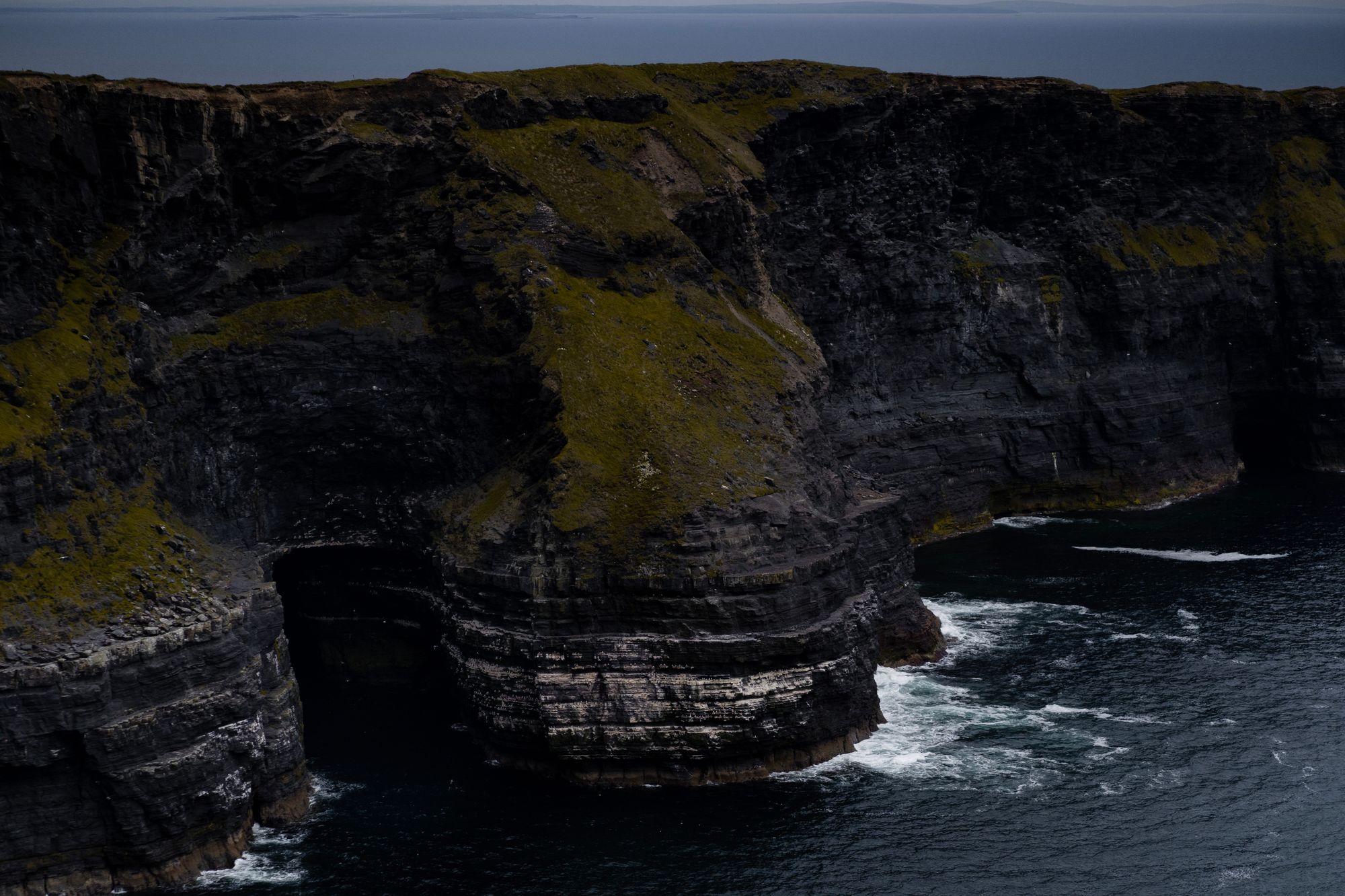 Dark sea cliffs covered in moss with waves breaking at their base