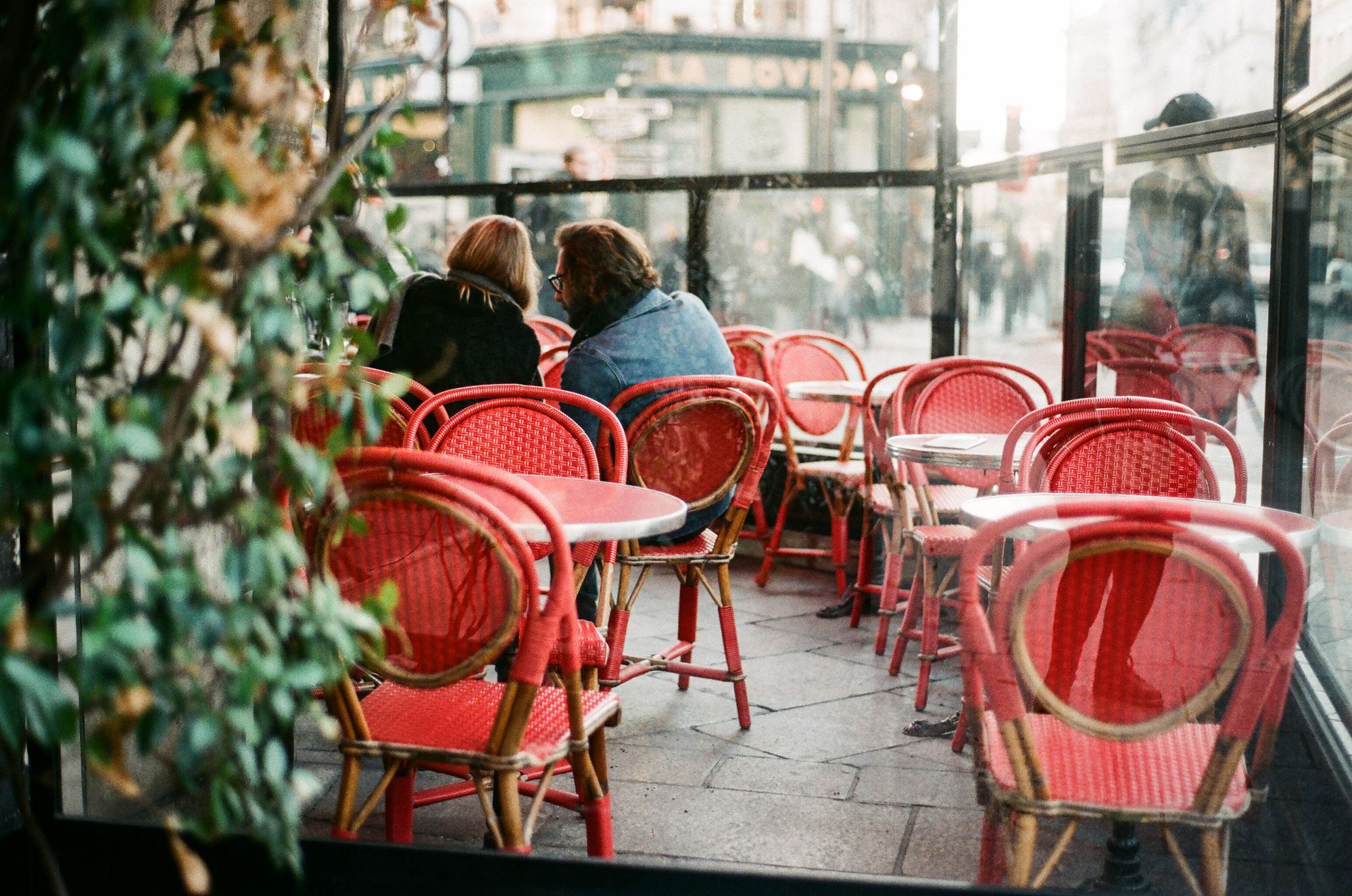 Red rattan chairs on a Paris café terrace with two people talking