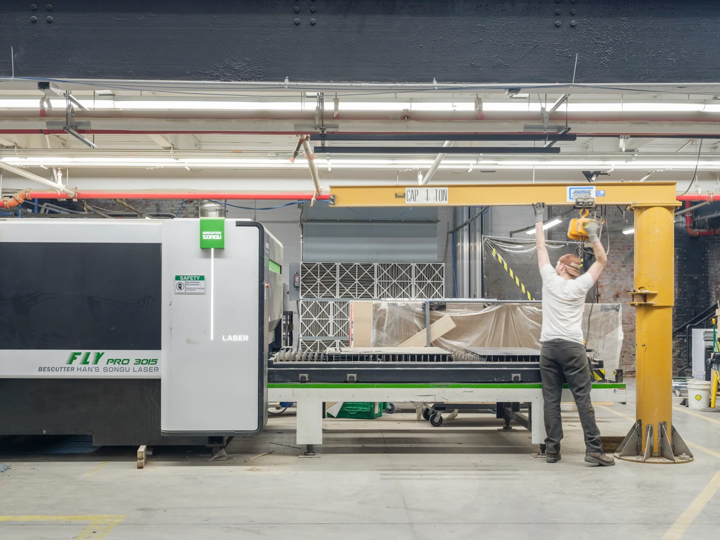 A Bednark worker at a jib crane hoist beside a fiber laser cutter